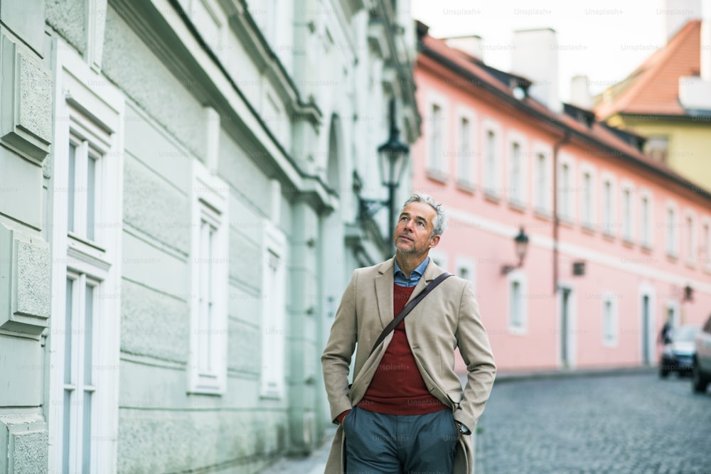 Um homem de negócios maduro andando em uma rua na cidade de Praga, com as mãos nos bolsos. Espaço de cópia.