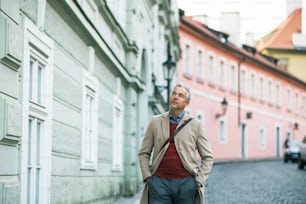 A mature businessman walking on a street in Prague city, hands in pockets. Copy space.