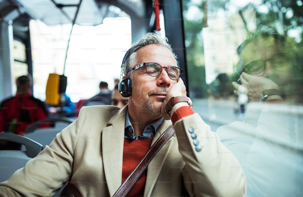 Reifer, müder Geschäftsmann mit Brille und Kopfhörern, der mit dem Bus durch die Stadt reist und Musik hört.