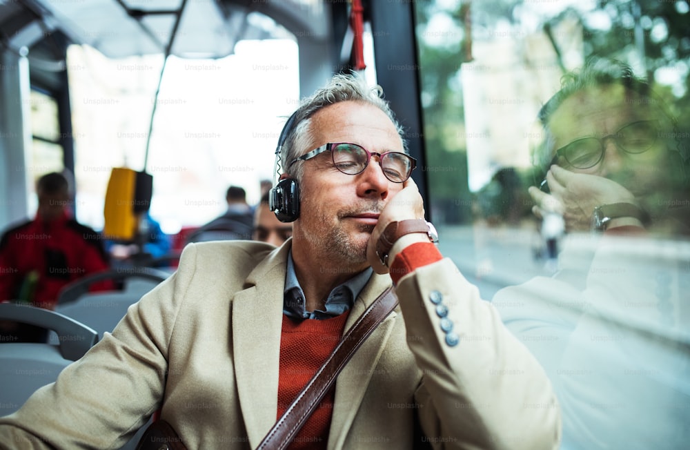 Homme d’affaires mature et fatigué avec des lunettes et des écouteurs voyageant en bus dans la ville, en écoutant de la musique.
