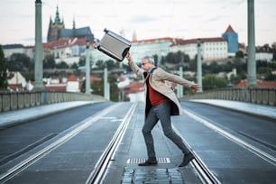 Ein glücklicher, reifer, gutaussehender Geschäftsmann mit Koffer, der eine Straße in Prag überquert.