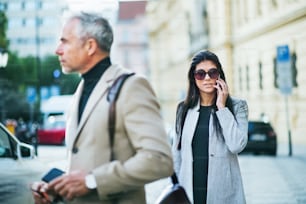 Mature man and young woman business partners walking outdoors in city of Prague.