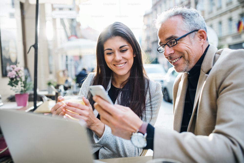 Un homme et une femme d’affaires partenaires avec un ordinateur portable et un smartphone assis dans un café de la ville, en train de parler.