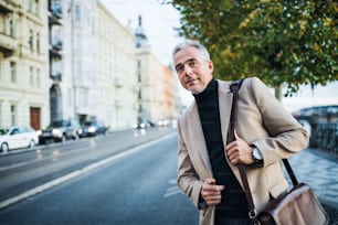 Mature businessman with bag standing on the street in city of Prague, waiting for a taxi cab. Copy space.