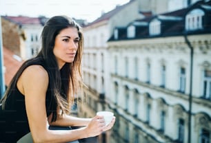 Happy young businesswoman with cup of coffee standing on a terrace in an office in city. Copy space.