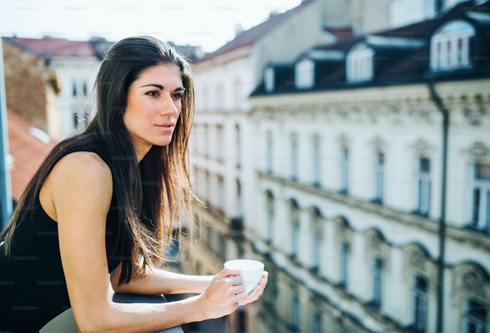 Giovane donna d'affari felice con la tazza di caffè in piedi su una terrazza in un ufficio in città. Copia spazio.