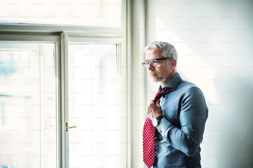 Mature businessman with glasses on a business trip standing in a hotel room, getting dressed. Copy space.