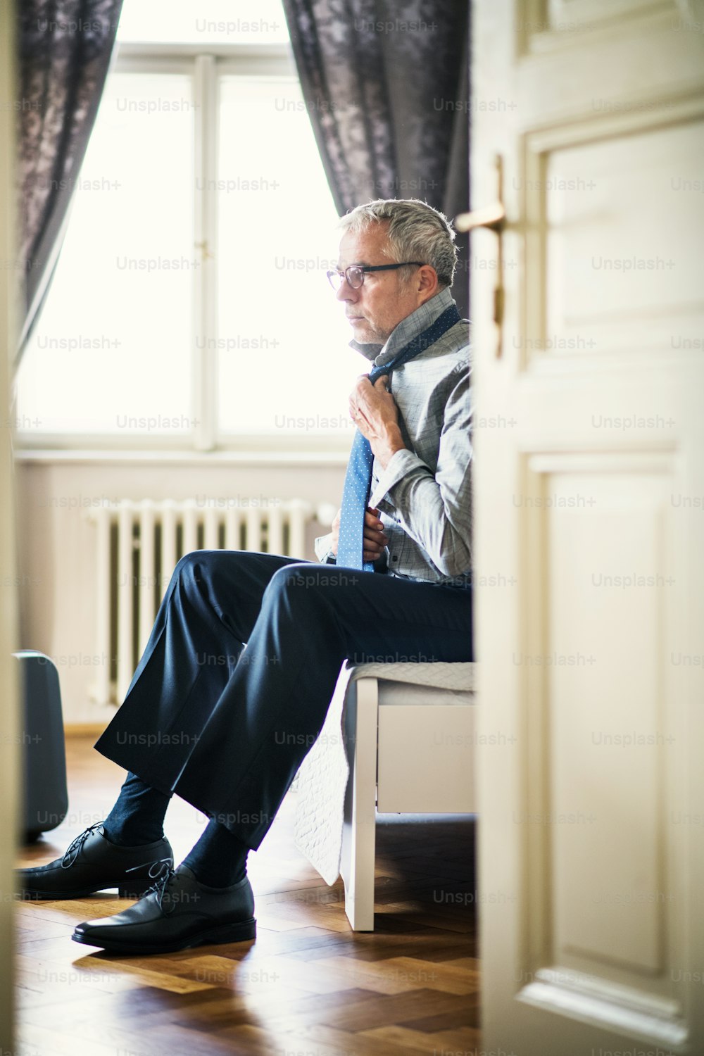 Mature businessman with glasses on a business trip in a hotel room, getting dressed.