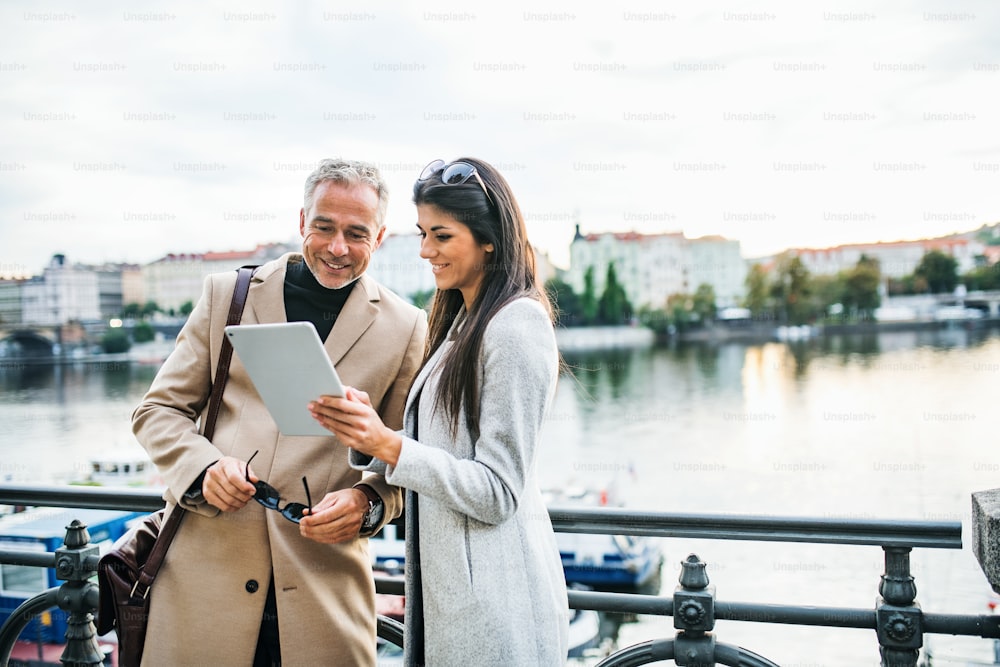 Man and woman business partners with tablet standing by a river in city of Prague, talking. Copy space.