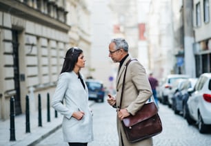 Un homme mûr et une jeune femme partenaires d’affaires debout à l’extérieur dans la ville de Prague, en train de parler.