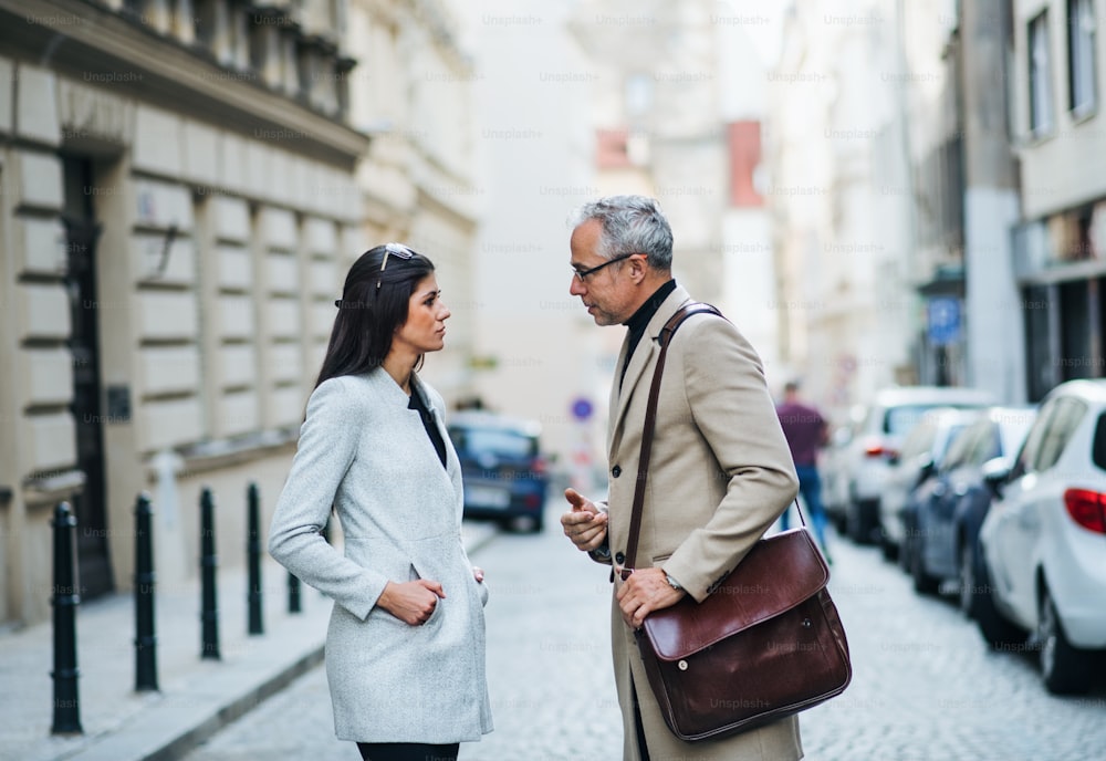 プラハの街で屋外に立って話す成熟した男性と若い女性のビジネスパートナー。
