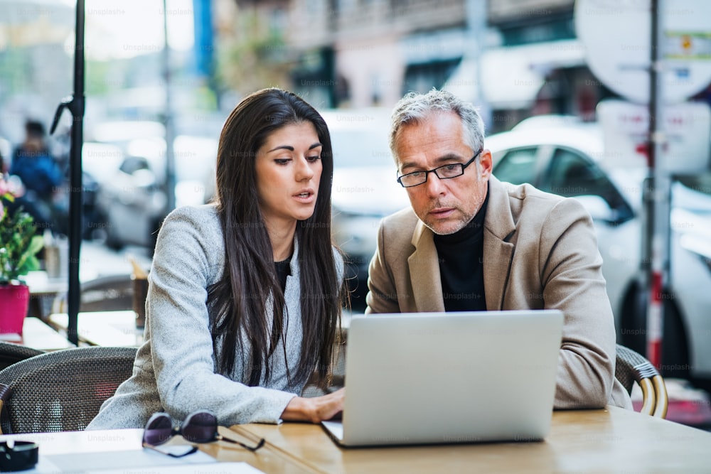Uomo e donna soci d'affari con laptop seduti in un caffè in città, discutendo di problemi.