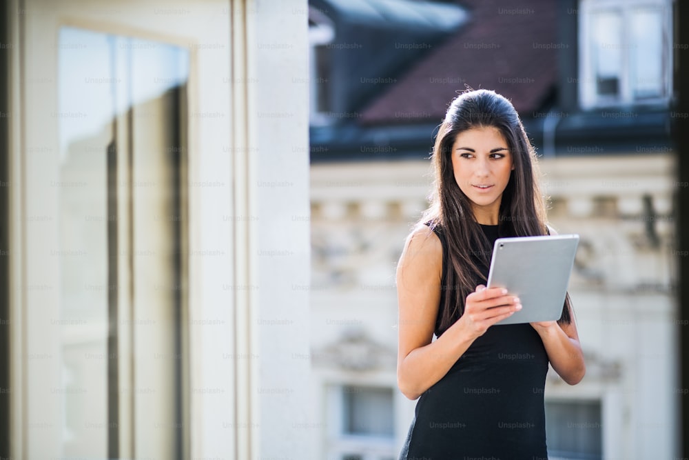 Giovane donna d'affari con tablet in piedi su una terrazza fuori da un ufficio in città. Copia spazio.