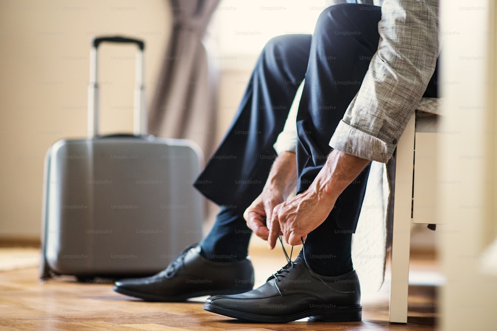 Vista de la sección media de un hombre de negocios maduro irreconocible en un viaje de negocios sentado en una habitación de hotel, atándose los cordones de los zapatos.