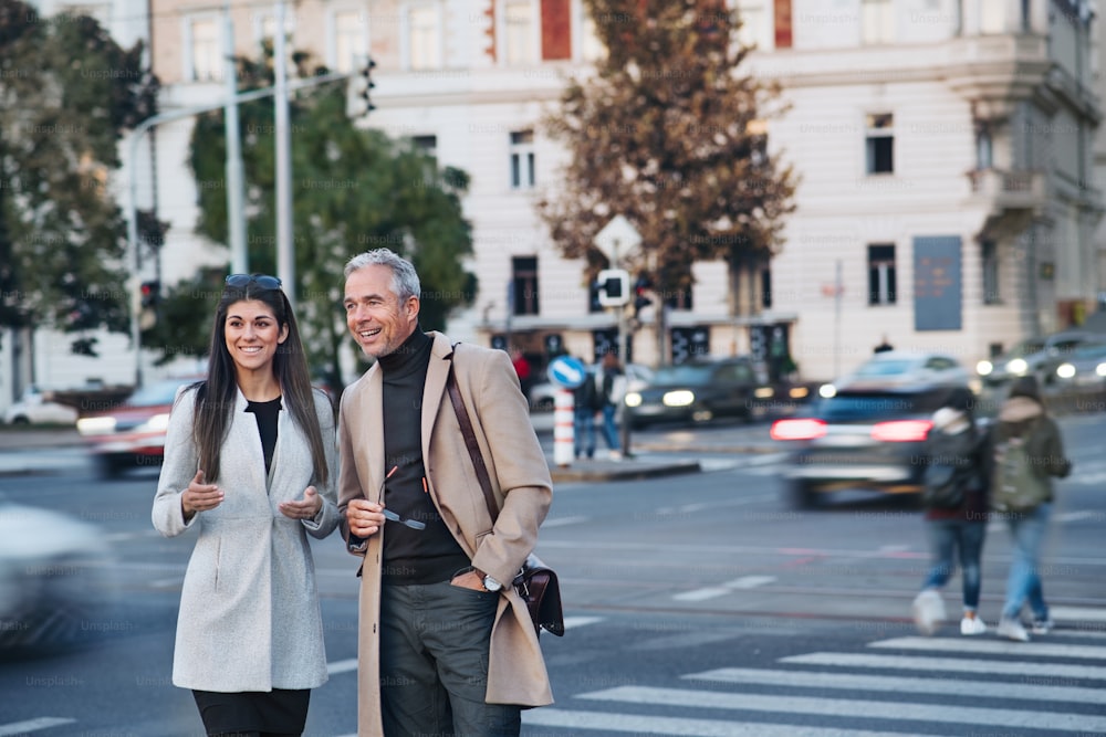 Cheerful man and woman business partners crossing road outdoors in city of Prague, talking. Copy space.