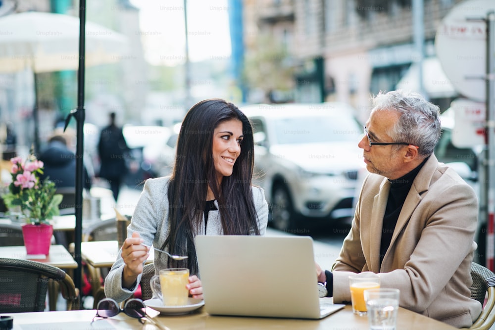 Uomo e donna soci d'affari con laptop e bevande seduti in un caffè in città, parlando.