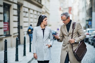 Mature man and young woman business partners walking outdoors in city of Prague, talking.