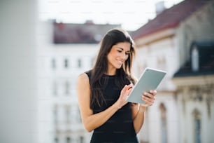 Young businesswoman with tablet standing on a terrace outside an office in city. Copy space.