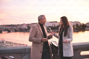 Cheerful man and woman business partners standing by a river in city of Prague at dusk, talking.