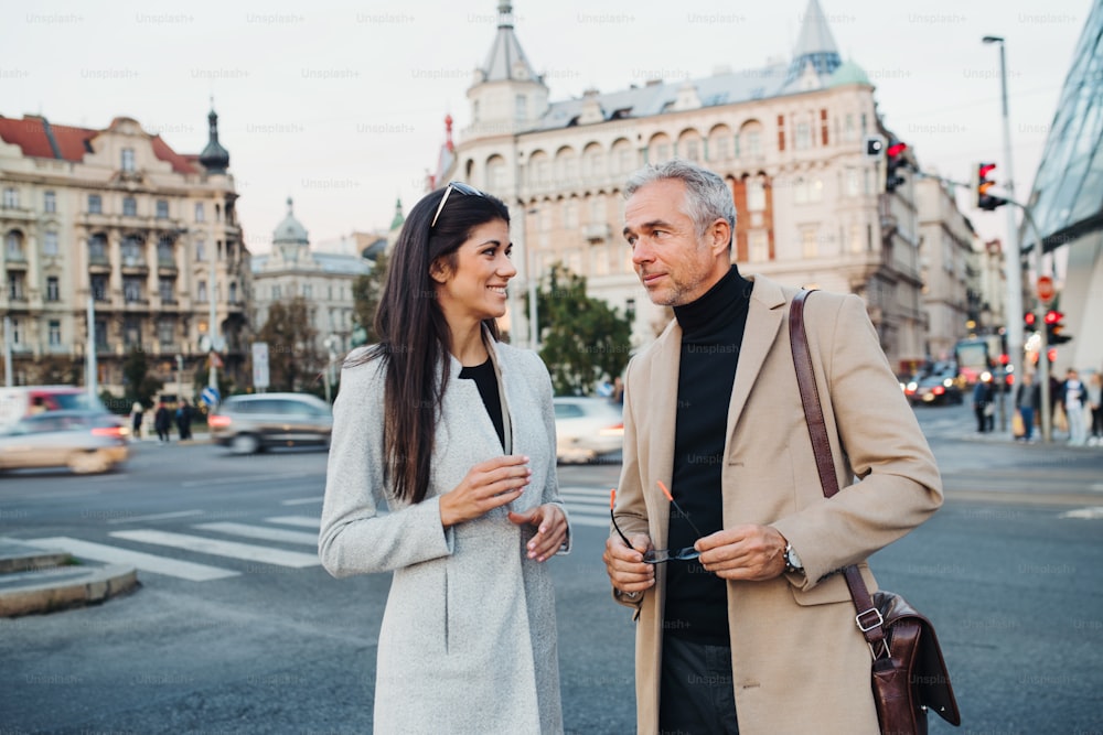 Mature man and young woman business partners standing outdoors in city of Prague, talking.