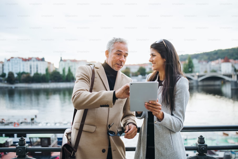 Mann und Frau Geschäftspartner mit Tablet stehen an einem Fluss in der Stadt Prag und unterhalten sich.
