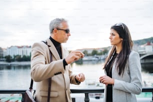 Mature man and young woman business partners standing by a river in city of Prague, talking.