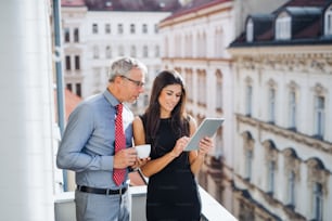 Homem e mulher parceiros de negócios com tablet em pé em um terraço no escritório na cidade, conversando.