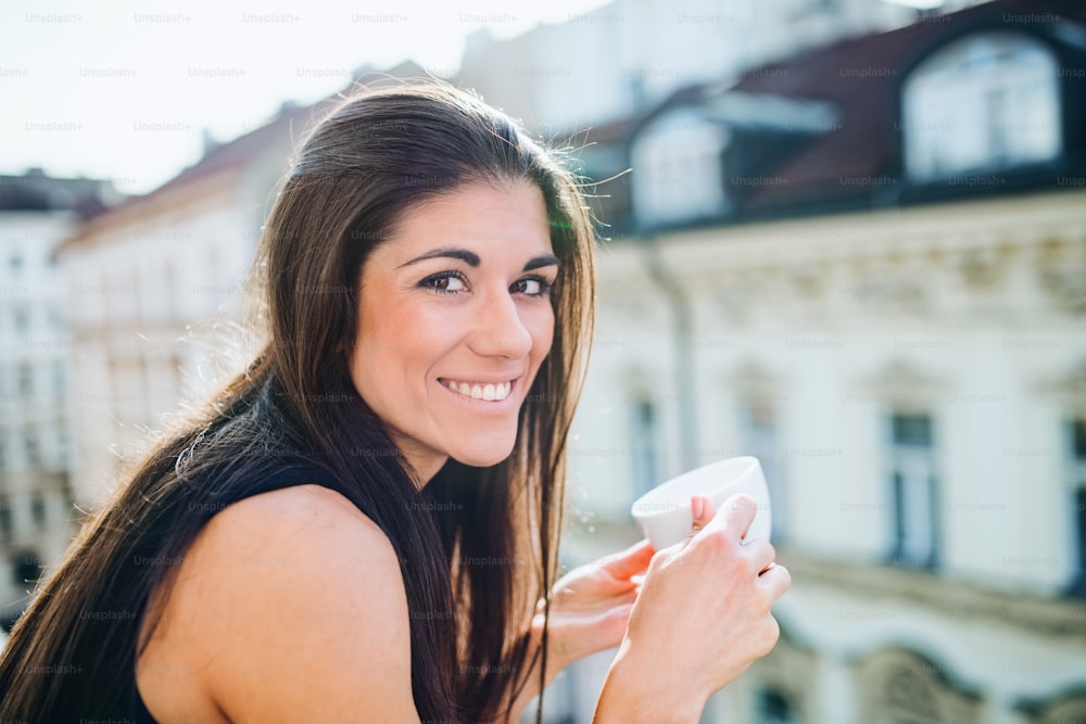 Giovane donna d'affari felice con la tazza di caffè in piedi su una terrazza in un ufficio in città.