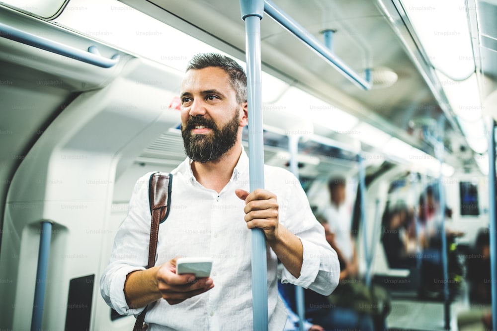 Uomo d'affari hipster con smartphone in piedi all'interno della metropolitana in città, in viaggio per andare al lavoro e inviare messaggi.