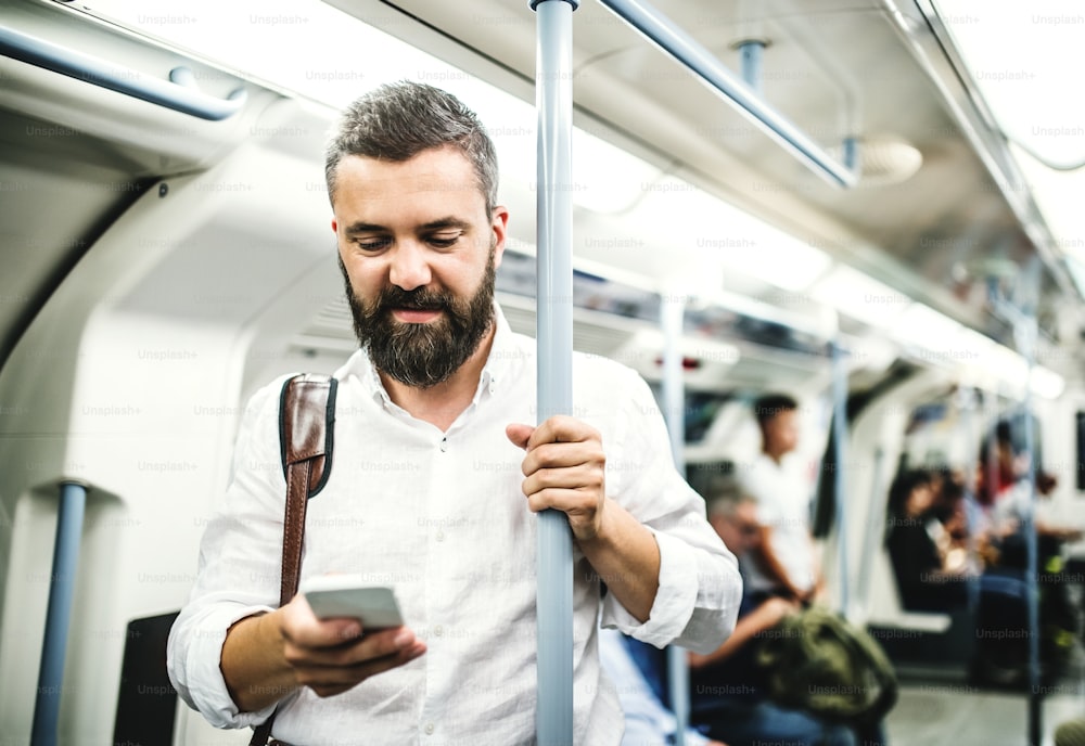 Hombre de negocios hipster con teléfono inteligente parado dentro del metro en la ciudad, viajando al trabajo y enviando mensajes de texto.