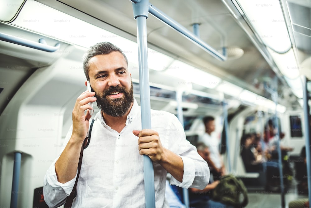 Uomo d'affari hipster con smartphone in piedi all'interno della metropolitana in città, in viaggio per andare al lavoro e fare una telefonata.