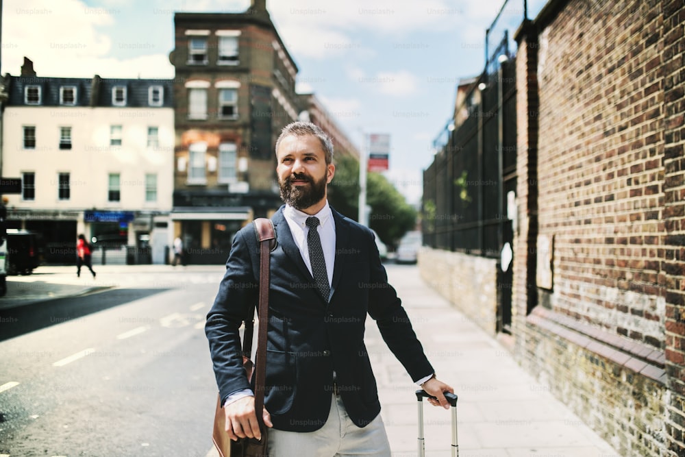 Hombre de negocios hipster con bolsa de computadora portátil y maleta caminando por la calle en Londres. Espacio de copia.