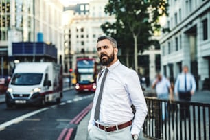 Hipster-Geschäftsmann steht auf der Straße in London neben einer stark befahrenen Straße, die Hände in den Taschen.