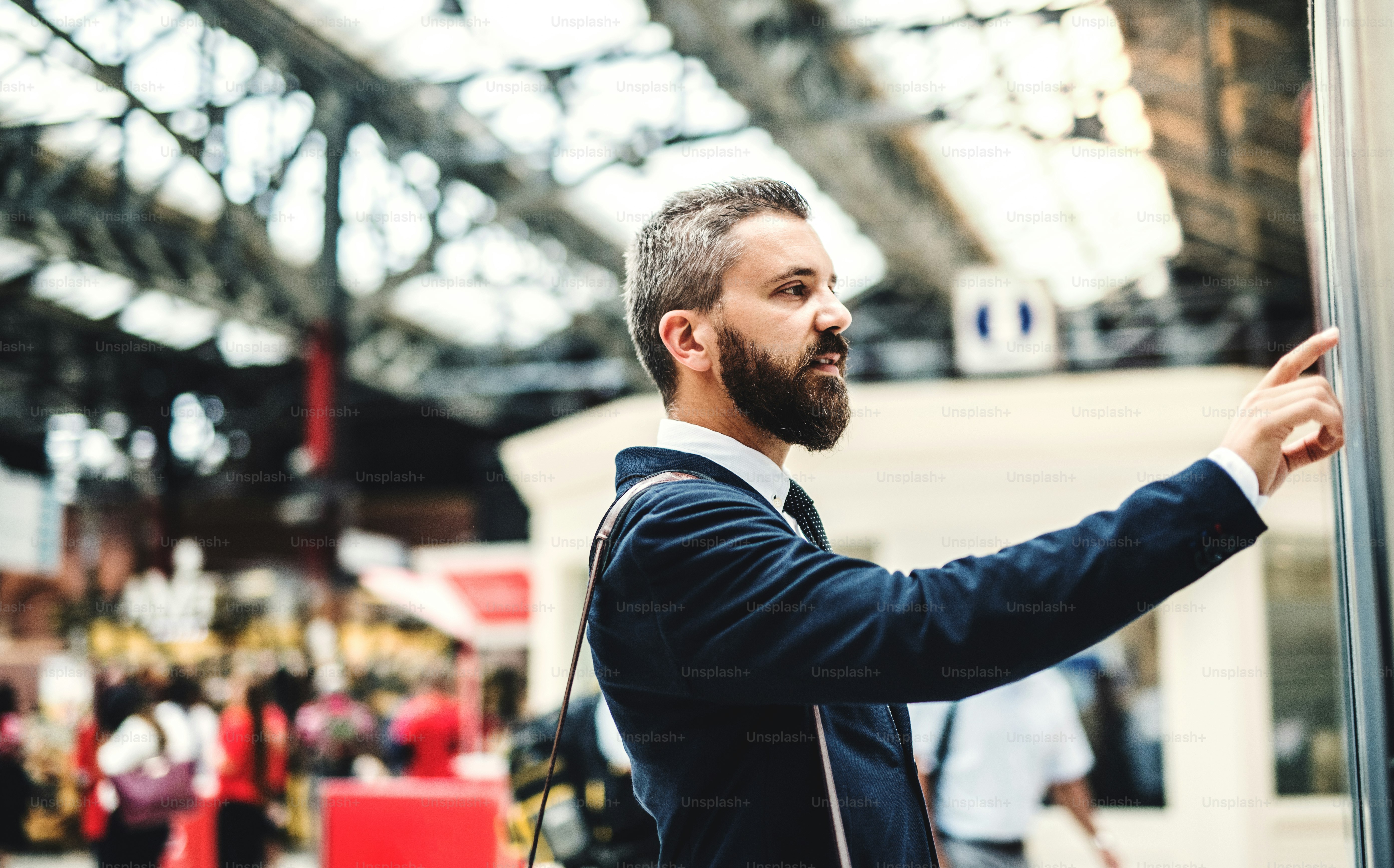 Vista lateral de un hombre de negocios hipster parado en la estación de autobús o tren, verificando el horario.