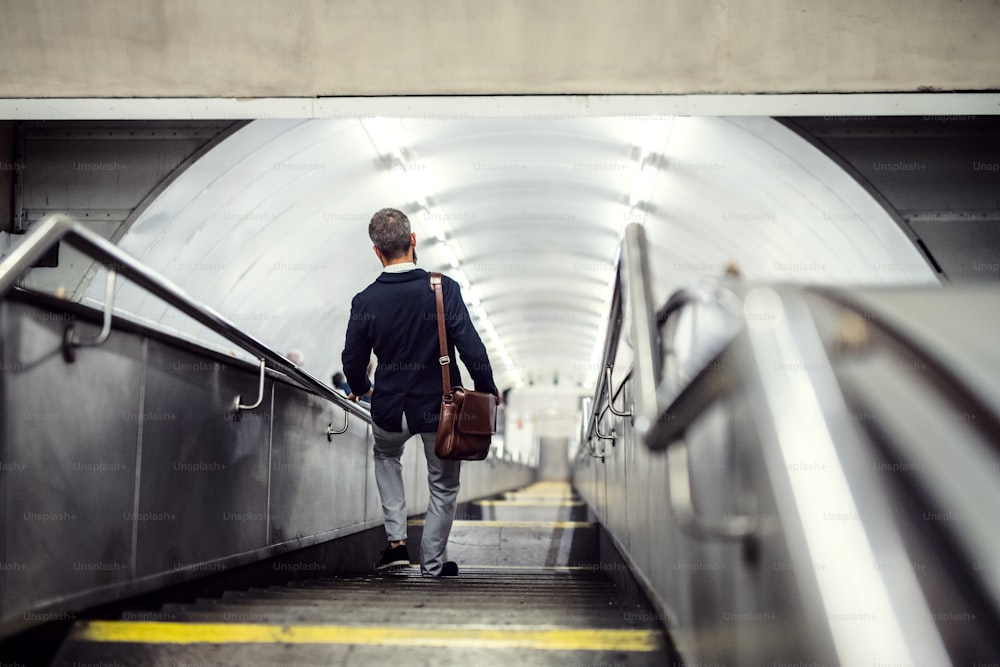 市内の地下鉄の階段を歩いて仕事に行く流行に敏感なビジネスマンの背面図。