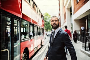 Ernsthafter Hipster-Geschäftsmann, der auf der Straße steht und in London auf den Bus wartet.