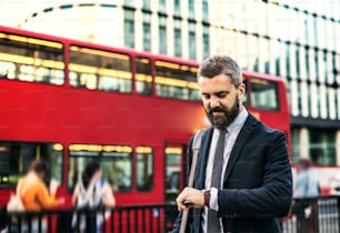 Hombre de negocios hipster esperando el autobús en la calle en Londres, comprobando la hora.