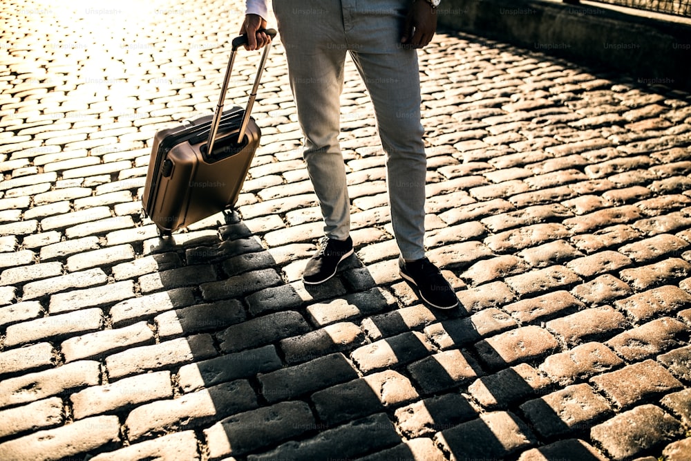 Legs of businessman with suitcase standing on a pavement on the street. Copy space.