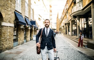 Hipster businessman with laptop bag and suitcase walking down the street in London. Copy space.