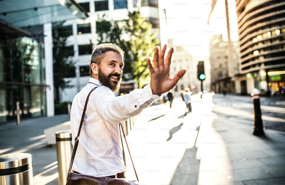 Vista trasera de un hombre de negocios hipster caminando por la calle en Londres, mirando hacia atrás y saludando a alguien. Espacio de copia.