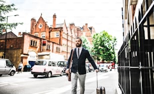Uomo d'affari hipster con borsa del computer portatile e valigia che cammina lungo la strada di Londra. Copia spazio.