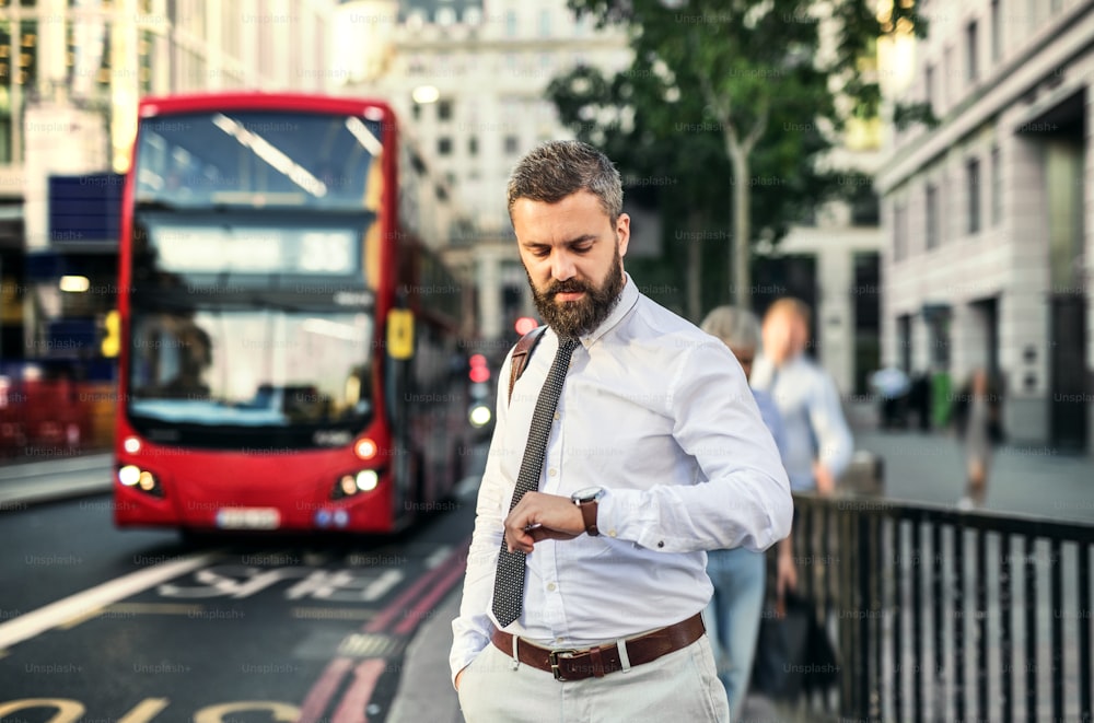 Hipster-Geschäftsmann, der auf der Straße in London auf den Bus wartet und die Uhrzeit überprüft.