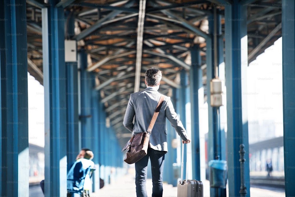 Belo empresário maduro em uma cidade. Homem andando na plataforma ferroviária na estação de trem. Vista traseira.