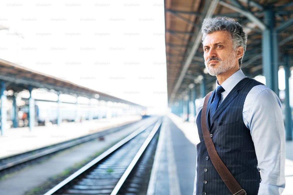 Gutaussehender reifer Geschäftsmann in einer Stadt. Mann, der am Bahnhof auf den Zug wartet.