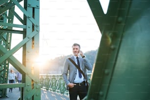 Handsome mature businessman with a smartphone in a city. Man walking on a bridge, making a phone call.