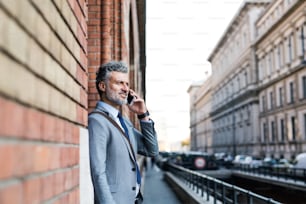 Gutaussehender reifer Geschäftsmann mit Smartphone in einer Stadt, der telefoniert.