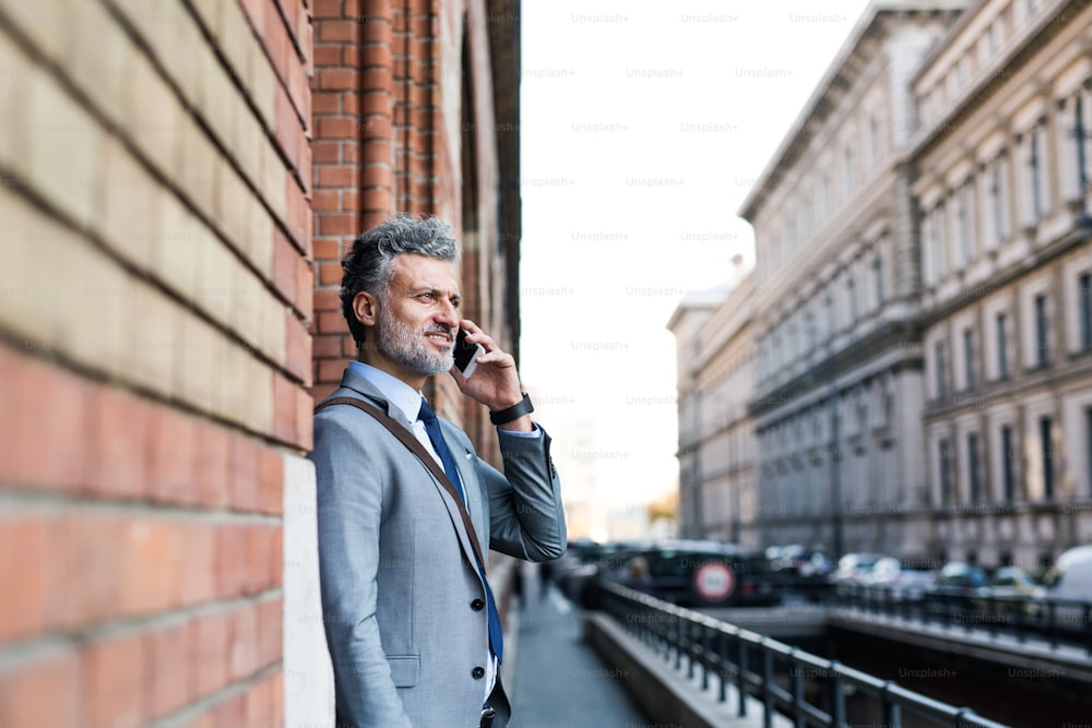 Guapo hombre de negocios maduro con teléfono inteligente en una ciudad, haciendo una llamada telefónica.