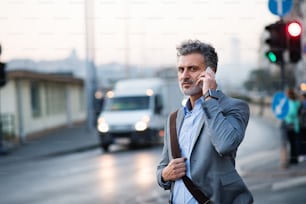 Handsome mature businessman with smartphone in a city, making a phone call.