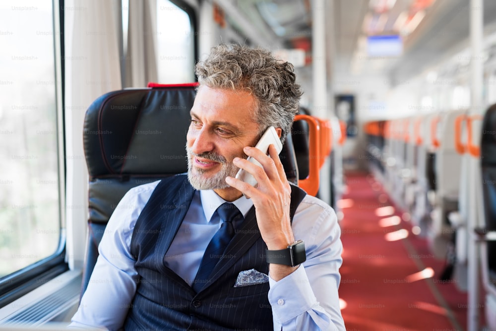 Bel homme d’affaires mûr voyageant en train. Un homme avec un smartphone, passant un appel téléphonique.