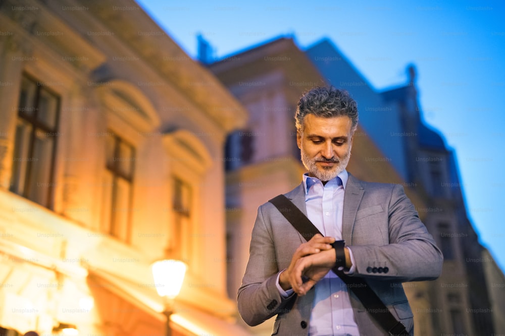 Handsome mature businessman with a smartwatch in a city in the evening, checking the time.